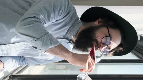 Pleased bearded man drinking red wine and admiring view form window at home. Stock Footage 155807747