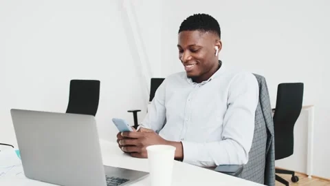 A pleased black guy with earbuds using his smartphone in the office Stock Footage 154360957