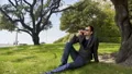 Pleased businessman talking on smartphone in park, sitting on grass near tree HD Footage