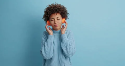 Pleased calm dark skinned young ethnic woman moves to rhythm of music closes Stock Footage 144917292