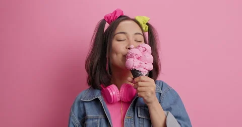 Pleased satisfied millennial girl with two pony tails licks delicious ice cream Stock Footage 154776953