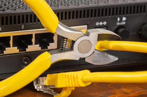 Pliers cutting a yellow ethernet cable plugged into a network router port clo Stock Photos
