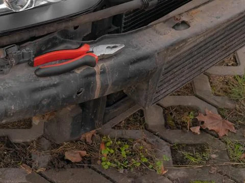 Pliers placed on a rusty car bumper with a headlight in view on a paved surfa Stock Photos