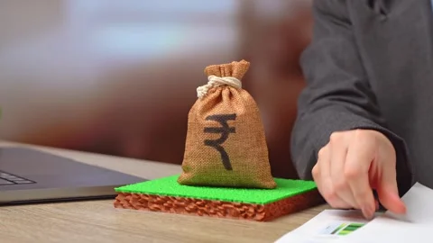 A plot of land and a indian rupee money bag. Investments in the land market. Stock Footage 346760758