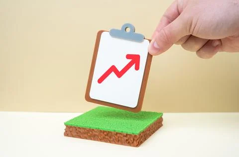 A plot of land and a tablet with a red arrow pointing upward. Rising land pri Stock Photos