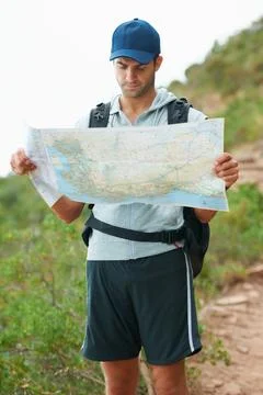 Plotting his next move. Handsome young hiker reading a map while standing on a Fotos de archivo
