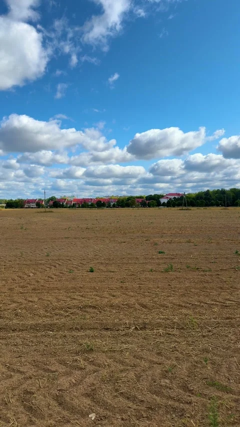 Plowed brown field under cloudy blue sky with red roof houses and trees Stock Footage 343406337