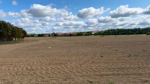 Plowed brown field under cloudy blue sky, rural landscape with houses  Stock-Footage 343406950