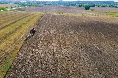 Plowing the ground with a tractor to which a plow is attached, aerial view. A Stock Photos