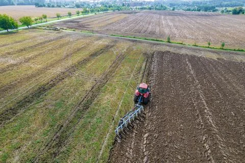 Plowing the ground with a tractor to which a plow is attached, aerial view. Stock Photos