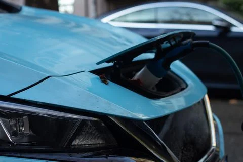 Plug is inserted into socket and tank of blue electric car at charging station Stock Photos