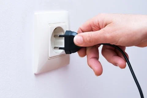 Plugging a black electrical plug into a wall socket with a woman's hand. Stock Photos