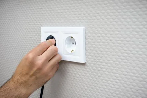 Plugging electrical, black plug in white electric socket on wall. Stock Photos