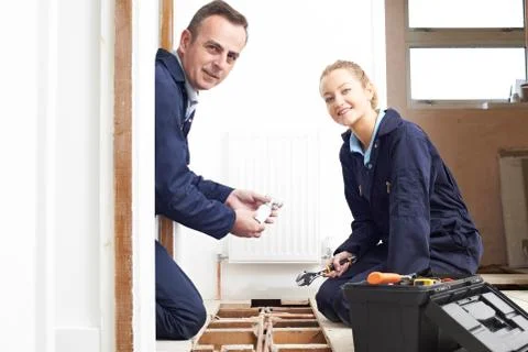 Plumber And Female Apprentice Fitting Central Heating System 库存照片