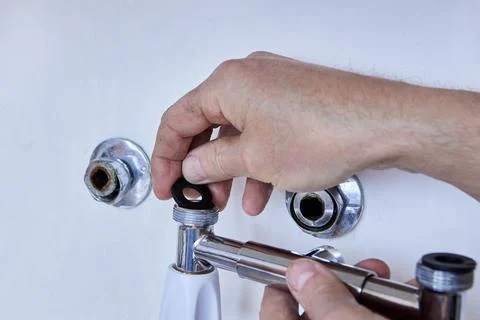 Plumber carefully aligns rubber gasket on threaded end of new mixer tap bef.. Stock Photos