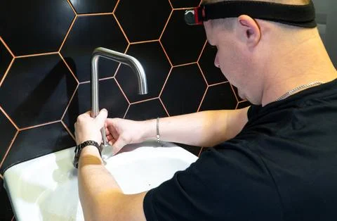 Plumber changes broken, leaking plumbing fixtures in the kitchen. Stock Photos