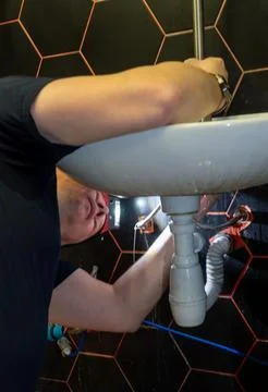 Plumber changes broken, leaking plumbing fixtures in the kitchen. Stock Photos