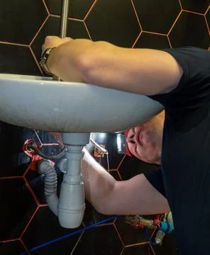 Plumber changes broken, leaking plumbing fixtures in the kitchen. Stock Photos