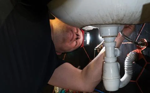 Plumber changes broken, leaking plumbing fixtures in the kitchen. Stock Photos