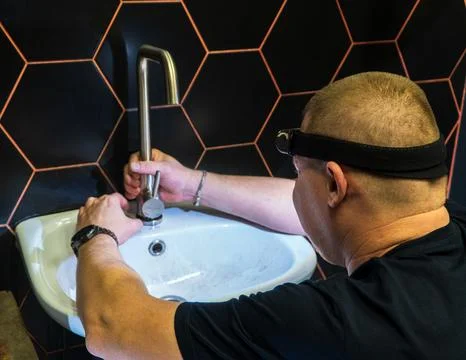 Plumber changes broken, leaking plumbing fixtures in the bathroom. Repair o.. Stock Photos