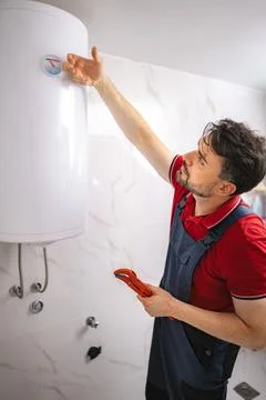 Plumber checking temperature of water heater and holding pipe wrench Stock Photos