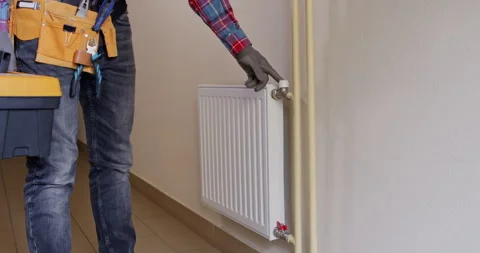 Plumber checks radiator valve alignment and tests shutoff Stockbeeldmateriaal 322010565