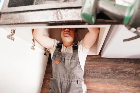 The plumber disassembles the siphon under the sink to clear the blockage. Stock Photos