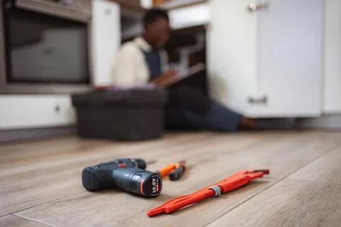 Plumber fixing kitchen sink using tools and writing notes Stock Photos
