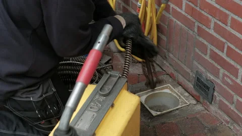Plumber inserts plumbing snake inside clogged drainage pipe Stock Footage 130658844