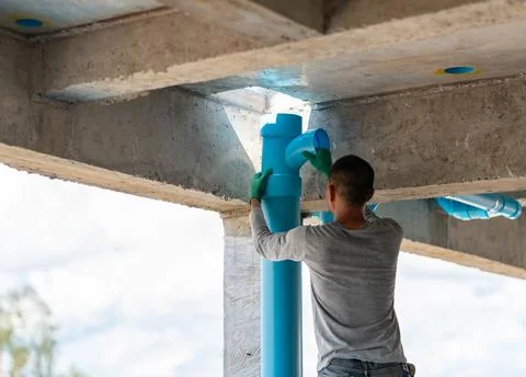 Plumber installing blue PVC drainage pipe fittings under a concrete slab at.. Stock Photos