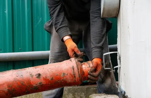 Plumber installing orange plastic sewage pipe outdoor. Worker in gloves fix.. Stock Photos