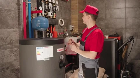 Plumber In Red Uniform Inspecting Boiler And Heating System Stock Footage 330859094