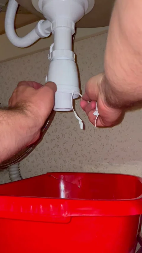Plumber repairing kitchen sink pipe. Workman is applying white sealant tape to Stock Footage 340124709