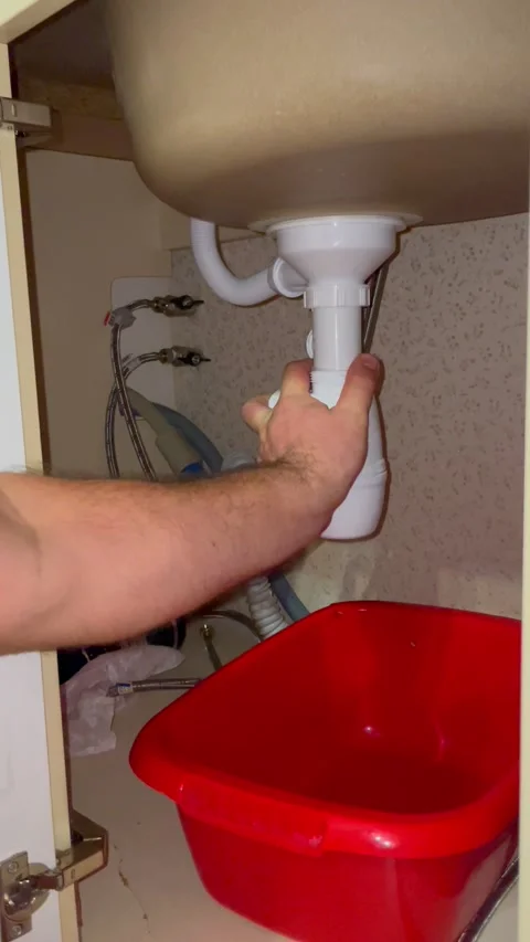 Plumber repairing sink drain pipe under kitchen cabinet. Man tightening white Stock Footage 340124691