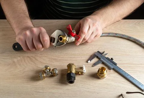 Plumber screws the brass fitting onto the valve with a plumbing wrench. Stock Photos