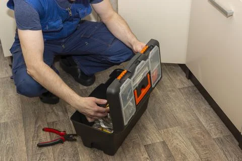 Plumber service worker digging in a toolbox at work in kitchen 库存照片