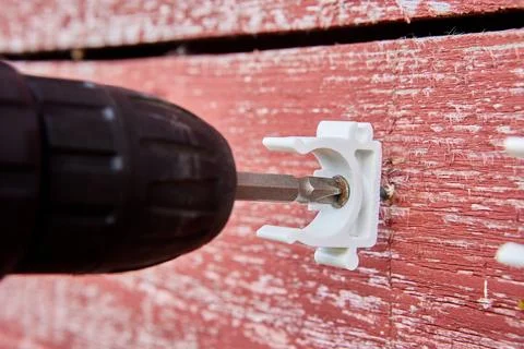 Plumber is using cordless drill to secure white pipe clips to weathered red Stock Photos