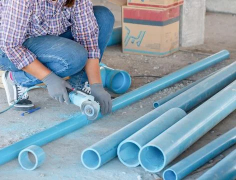 A plumber using an electric angle grinder to precisely cut blue PVC water p.. Stock Photos
