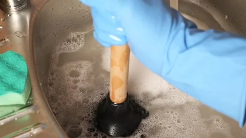 Plumber using plunger to unclog a kitchen sink drain Stock Footage 345530364