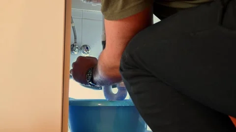 Plumber working on a leaking sink pipe under a cabinet Stock Footage 335512627