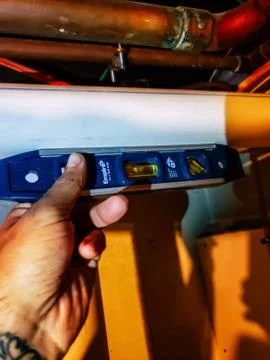 Plumbers hand using a level to pitch HVAC pvc piping. Stock Photos