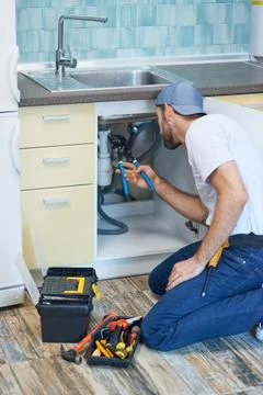 Plumbing troubles. Professional plumber using pipe wrench while examining and Stock Photos