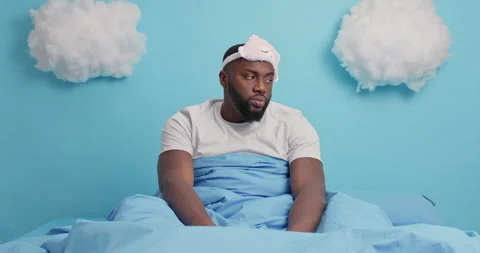 Plump bearded dark skinned man stretches in bed awakes very early yawns at Stock Footage 148995200
