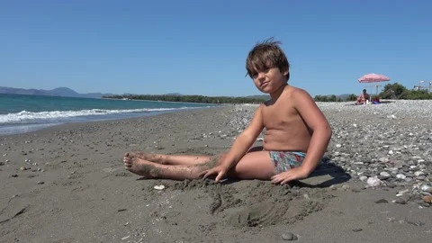 Plump boy plays in the sand at the beach Stock Footage 141835926