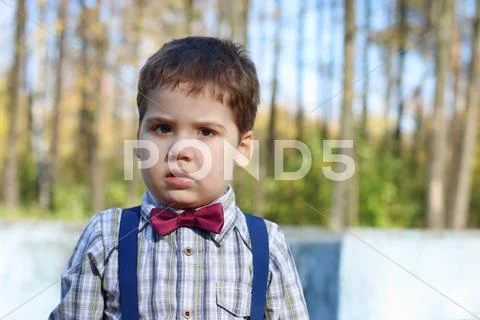 Plump little boy in shirt and bow tie looks at camera in sunny green park Stock Photos