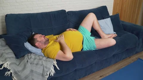 Plump man with beard in yellow T-shirt is lying on bed at home and stroking big 動画素材 170608774