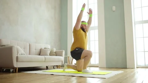 Plump man doing squats in lunges exercise with hands up standing on mat at home. Stock Footage 148993477