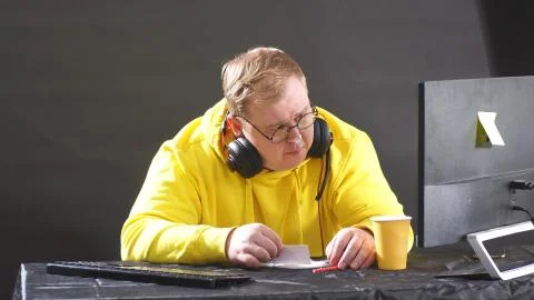 Plump man in a yellow jacket is sitting at a computer on an isolated black Stock Photos