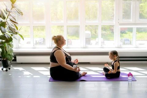 Plump mother and a fragile, thin daughter are doing yoga at home Stock Photos