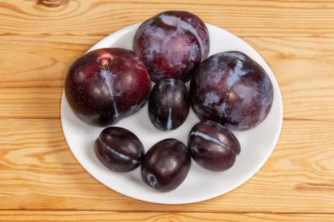 Plums different varieties and sizes on plate on rustic table Stock Photos